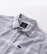 Camisa de franela de manga larga con estampado de cuadros en blanco y negro. Presenta cuello inglés, cierre frontal con botones y bolsillo en el pecho.