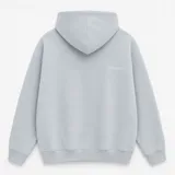 Canguro con capucha de calce oversize, confeccionado en tejido pesado color gris claro. Presenta un bordado minimalista con la palabra 'ASCEND' en la parte superior trasera, puños y ruedo acanalados.