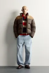 Cazadora puffer relaxed fit color marrón con canesú superior en tono tostado de acabado aterciopelado. Cuenta con cuello subido, manga larga, bolsillos de vivo en la cadera, acabados en elástico y cierre frontal con cremallera.