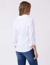 Camisa blanca entallada de algodón con escote en V y cuello con solapa. Presenta un diseño frontal con alforzas horizontales en la pechera y mangas tres cuartos con puños anchos rebatibles.
