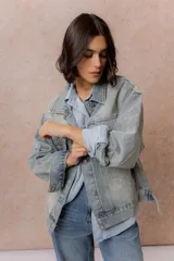 Campera de denim oversized en lavado celeste, con hombros caídos, cierre frontal con botones metálicos, bolsillos delanteros con tapa y aplicaciones de strass con diseño orgánico en delantero, mangas y espalda.