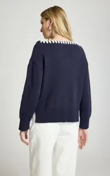Sweater azul marino de tejido de punto con escote barco, detalle contrastante en color blanco a lo largo del borde, mangas largas con hombros caídos y ajuste ligeramente holgado.