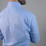 Camisa de vestir celeste de manga larga, con cuello clásico y botones blancos. Presenta un logo bordado en azul oscuro en el pecho.