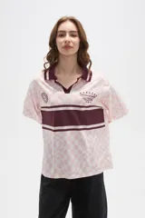 Remera tipo chomba de manga corta con cuello camisero, confeccionada en tejido con estampado de tablero ondulado en tonos rosado y blanco, con franja horizontal y detalles gráficos en color bordó.