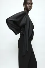 Blusa negra de satén con escote fluido, diseño drapeado en el frente y mangas largas anchas. Presenta un bajo asimétrico y una caída suave y elegante.