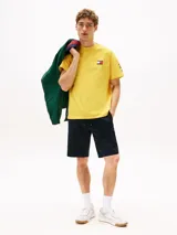 Remera amarilla de algodón con corte amplio, cuello redondo y hombros caídos. Presenta un logo pequeño de Tommy Hilfiger en el pecho, un logo en la manga y un logo grande en la espalda. Pertenece a la colección Hilfiger Sailing.