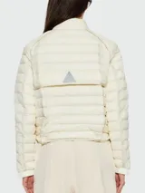 Campera acolchada Moncler modelo Madulains, color blanco hueso, con cuello alto, cierre frontal con botones a presión y diseño ligero. Presenta detalles de costuras horizontales y logo de la marca en la manga.