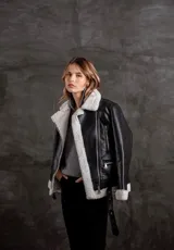 Campera tipo gamulán de cuero sintético negro con interior y solapas de corderito sintético en color blanco. Presenta cierre frontal, bolsillos laterales con cierre y cinturón ajustable en la cintura.