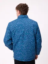 Campera reversible de nylon con cuello alto y cierre frontal. Un lado es de color gris liso con logo bordado, mientras que el otro lado presenta un estampado abstracto en tonos azules. Cuenta con bolsillos laterales y puños elásticos.