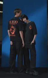 Remera de manga corta con cuello redondo y calce oversize, color negro con efecto nevado. Presenta una estampa frontal en color naranja con diseño gráfico de un rostro rodeado de llamas y texto tipográfico.