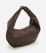 Bolso tipo baguette de formato curvo, confeccionado en poliuretano con acabado que imita el cuero. Presenta una estructura flexible con asa integrada y cierre superior metálico aparente que recorre el contorno.