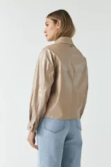Chaqueta color beige de cuero sintético con cuello clásico, cierre frontal con botones, bolsillos tipo parche en el pecho y corte holgado.