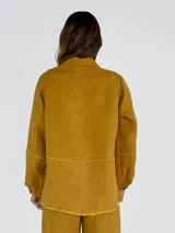 Chaqueta color amarillo de lino, con cuello camisero, cierre frontal con botones, mangas largas con puños abotonados y dos bolsillos de parche en el pecho.