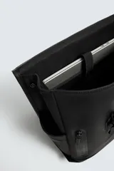 Mochila negra con acabado engomado, solapa con hebilla de liberación rápida, compartimento principal con espacio para dispositivos de hasta 13 pulgadas y bolsillo con cremallera, bolsillo frontal con cremallera, parte posterior acolchada con banda de sujeción para equipaje, asa de mano y dos asas de hombro ajustables y acolchadas.