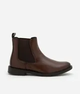 Bota tipo Chelsea de caña media, confeccionada en cuero sintético color marrón oscuro. Presenta punta redonda, paneles laterales elásticos para facilitar el calce y suela de goma robusta.