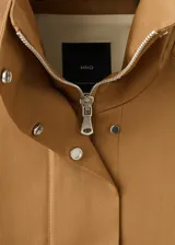 Chaqueta oversize color tostado con cuello embudo, manga larga, bolsillos laterales y bolsillos de parche con solapa. Cuenta con cierre delantero de cremallera y botones ocultos bajo tapeta, y forro interior.