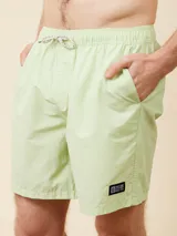 Short de baño tipo volley de color verde claro, con cintura elástica y cordón ajustable. Cuenta con un diseño liso y minimalista.