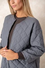 Campera acolchada de corte amplio y largo midi, color beige con diseño capitoneado. Presenta mangas tres cuartos con puños vueltos que revelan un interior estampado con motivo animal print. Diseño sin cuello y cierre frontal oculto.