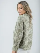 Blusa verde militar con estampado de flores blancas, cuello camisero, mangas largas con puños abotonados y cierre frontal con botones.