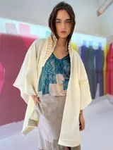 Ruana color crudo tejida en lana merino con cuello plisado a mano y terminaciones en fieltro de lana.