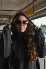 Canguro negro con capucha, corte oversize y diseño con hombros caídos. Presenta detalles bordados en la espalda con la palabra "Dual" en tipografía cursiva junto a texto descriptivo en tonos monocromáticos.