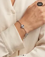 Pulsera de acero con cadena de eslabones finos y dijes colgantes en forma de flor de cuatro pétalos con textura estriada.