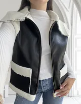 Chaleco negro de ecocuero con interior de corderito blanco, cierre frontal con cremallera y bolsillos laterales.
