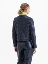 Chaqueta de cuero vacuno azul marino con diseño matelaseado, cuello camisero, cierre frontal con botones metálicos y bolsillos frontales superiores e inferiores.