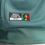 Campera deportiva Adidas con cierre frontal, cuello alto, mangas largas con las icónicas tres tiras blancas y puños elásticos. Presenta el logo de Adidas en el pecho derecho, la palabra 'Bob' bordada en el pecho izquierdo y un parche conmemorativo en la parte inferior derecha.