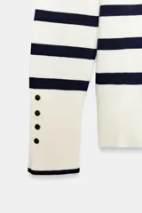 Jersey Zara de punto liso color negro, con cuello redondo, manga larga y detalle de botones dorados en los puños.