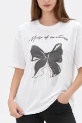 Remera blanca de algodón de manga corta, con cuello redondo y corte holgado. Presenta estampado frontal de un lazo con detalles de brillos y la frase 'Made of sweetness'.