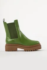 Bota tipo chelsea con suela track de goma en color marrón y capellada de cuero negro. Presenta elásticos laterales y tirador trasero.