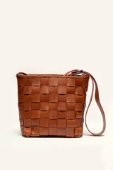 Cartera tipo morral de cuero color beige, con diseño trenzado artesanal, correa larga regulable y cierre superior.