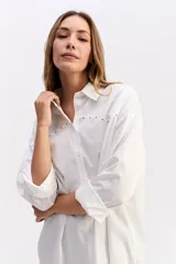 Camisa de algodón color blanco, de corte relajado y estilo western. Presenta detalle de tachas metálicas en la parte superior delantera y mangas largas con puños.