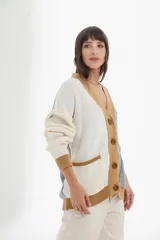 Cárdigan tejido de punto grueso, con diseño color block en gris, blanco y beige. Tiene cuello en V, cierre frontal con botones y un bolsillo de parche.