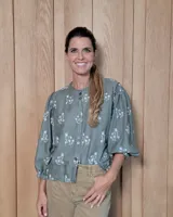 Camisa de color verde oliva con estampado floral blanco, cuello redondo, cierre frontal con botones y mangas tres cuartos abullonadas con puños elásticos.