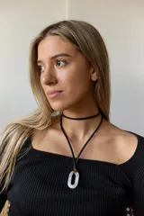 Collar con doble tira de tiento negro, una ajustada al cuello como choker y otra más larga con un dije ovalado de piedra natural blanca y un pequeño detalle dorado.