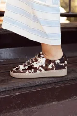 Sneaker de diseño artesanal confeccionada en cuero con pelo natural con estampado de manchas tipo vaca en tonos marrón y blanco. Presenta cordones al tono y suela de goma color caramelo.