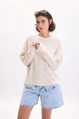 Sweater de punto fantasía color crudo, de corte holgado, con cuello redondo y mangas largas.