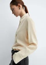 Camisa color crema de corte recto, cuello camisero y mangas largas con puños abotonados.