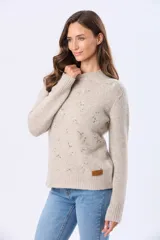 Buzo tejido de punto en color beige, con cuello redondo, mangas largas y puños acanalados. Presenta un delicado diseño bordado con motivos florales dispersos en el frente y una etiqueta de cuero sintético en el ruedo.