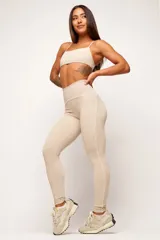 Calza deportiva de cintura alta color beige con detalles de vivos blancos a lo largo de las piernas.