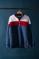 Buzo de felpa con medio cierre, diseño a bloques de color azul, blanco y rojo.