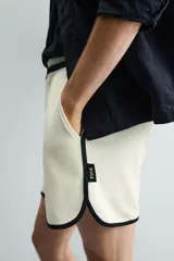 Short deportivo de tejido de punto con estructura abierta, color blanco con vivos a contraste en azul marino. Presenta cintura elástica, bolsillos frontales, aberturas laterales en el bajo y etiquetas conmemorativas de la Copa Mundial de la FIFA Francia 98.