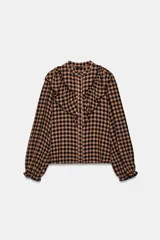 Blusa de manga larga con estampado de cuadros vichy en tonos marrón y negro. Presenta cuello redondo, cierre frontal con botones y detalle de volantes en el pecho.