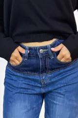 Pantalón de jean de corte recto y tiro alto, con diseño patchwork que combina diferentes tonos de denim azul y negro. Presenta bolsillos delanteros funcionales y cierre frontal con botón.