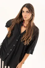 Camisa negra de corte oversize con diseño de encaje calado, escote en V, cierre frontal con botones y mangas tres cuartos. Presenta un diseño asimétrico con la parte posterior ligeramente más larga.