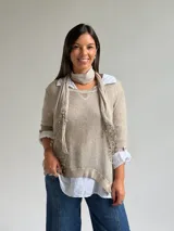 Sweater de punto fino en color beige, con cuello redondo y mangas tres cuartos. El diseño incluye una bufanda integrada del mismo tejido con detalles de puntilla en los extremos.