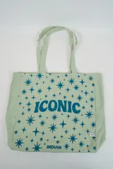 Bolso tote de tela con estampado de rayas verticales rosadas y blancas, laterales y asas en color beige. Presenta la palabra "BONJOUR" en verde en el centro y "INDIAN" en la parte inferior.