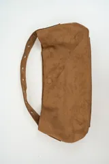 Bolso tipo baguette de gamuza color marrón, con correa ajustable mediante hebilla y cierre magnético central.